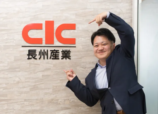 長州産業のロゴの前でポーズをとる