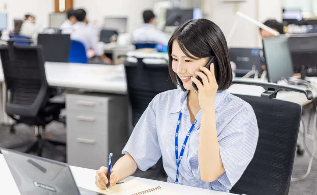 パソコンの前でメモを取りながら電話をする様子